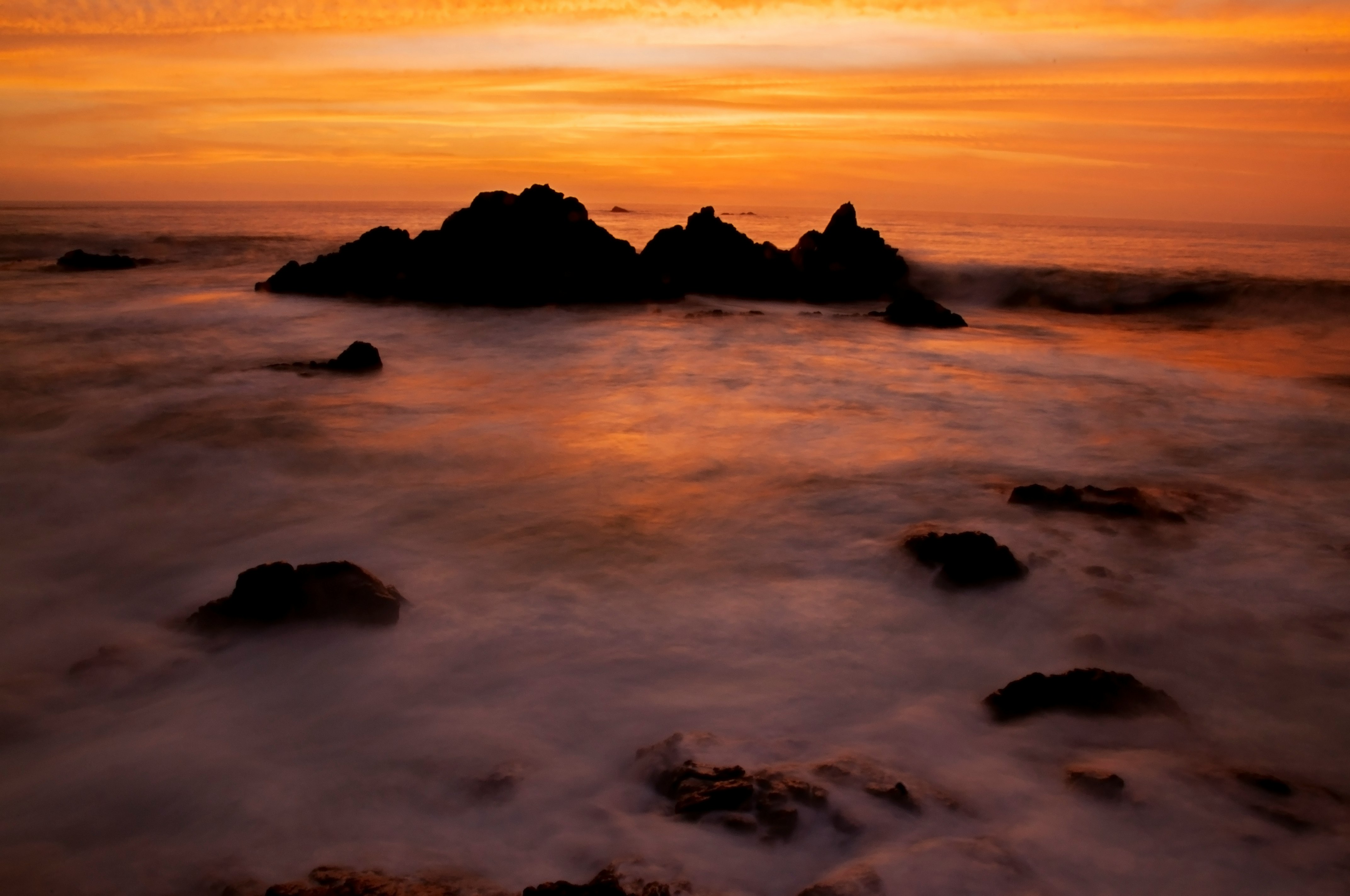 silhouette of rock formation on sea during sunset